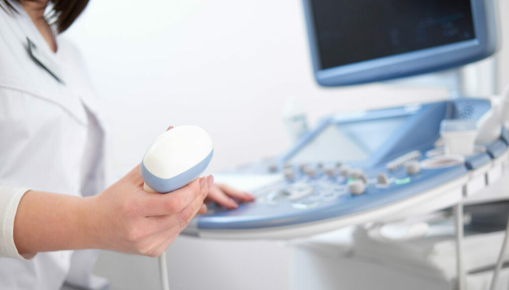ręka trzymająca końcówkę aparatu usg, w tle sprzęt diagnostyczny